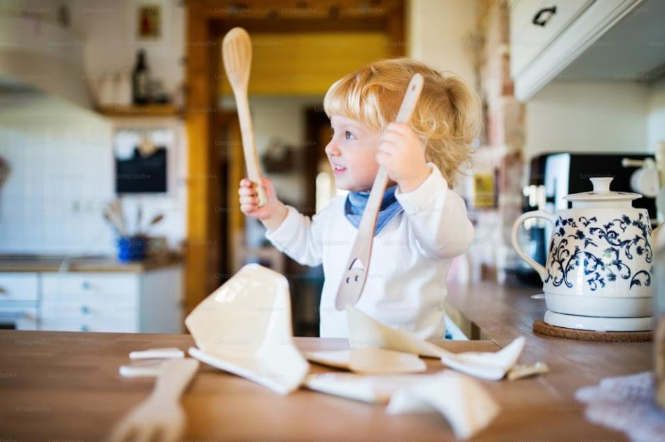 Kindje in keuken met keukengerei in de handen en gebroken pot op het aanrecht