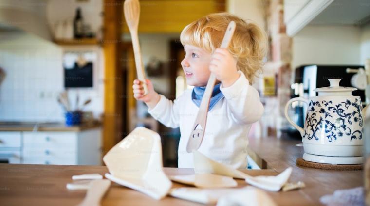 Kindje in keuken met keukengerei in de handen en gebroken pot op het aanrecht
